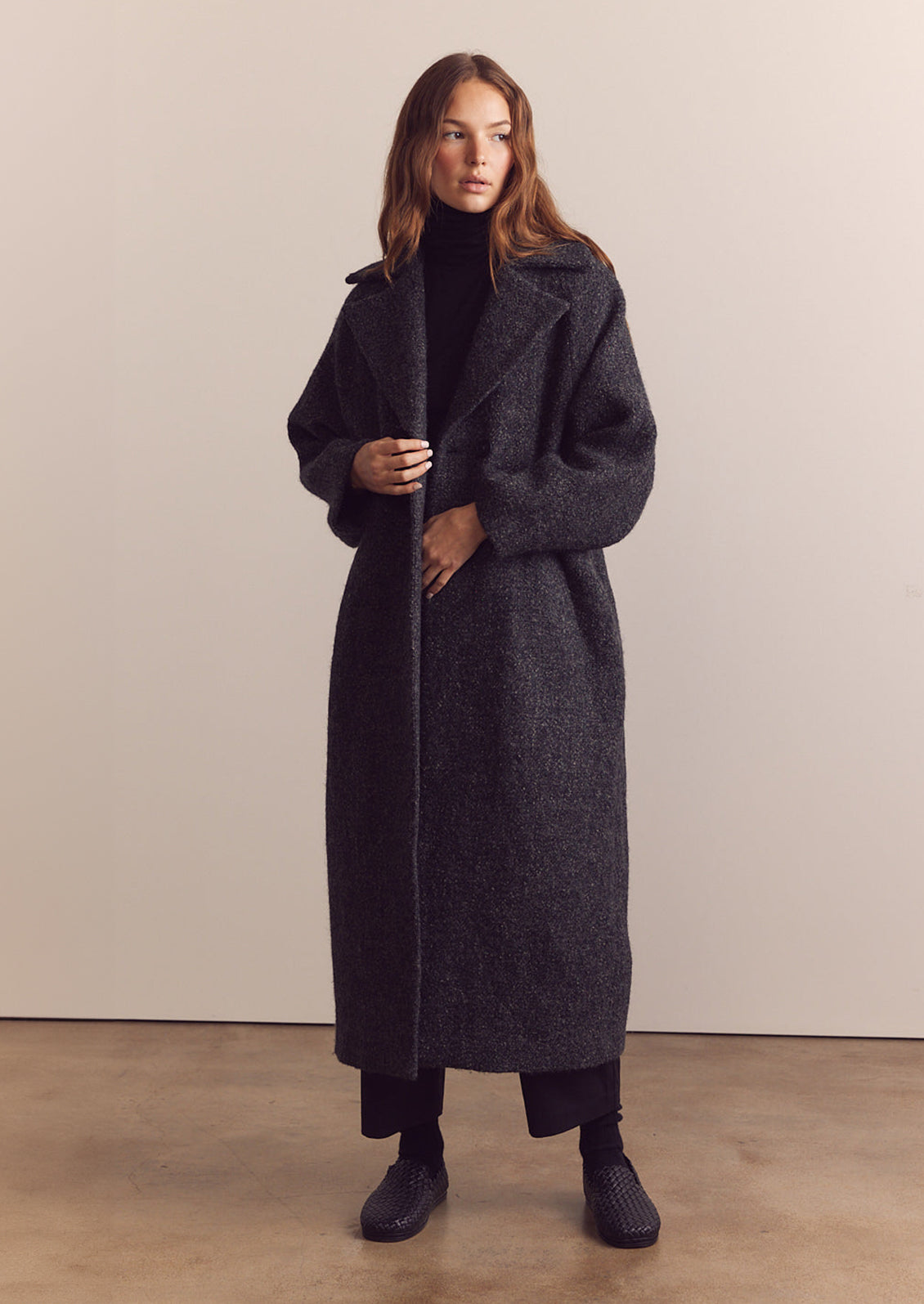 A woman wearing a long wool coat in dark grey speckled wool.