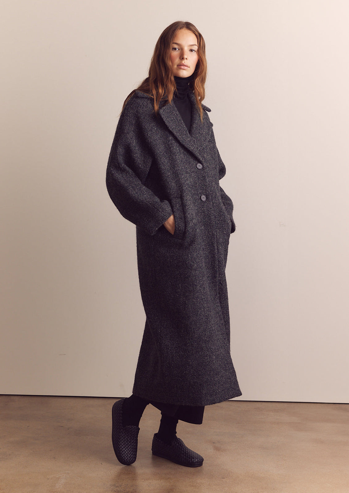 A woman wearing a long wool coat in dark grey speckled wool.