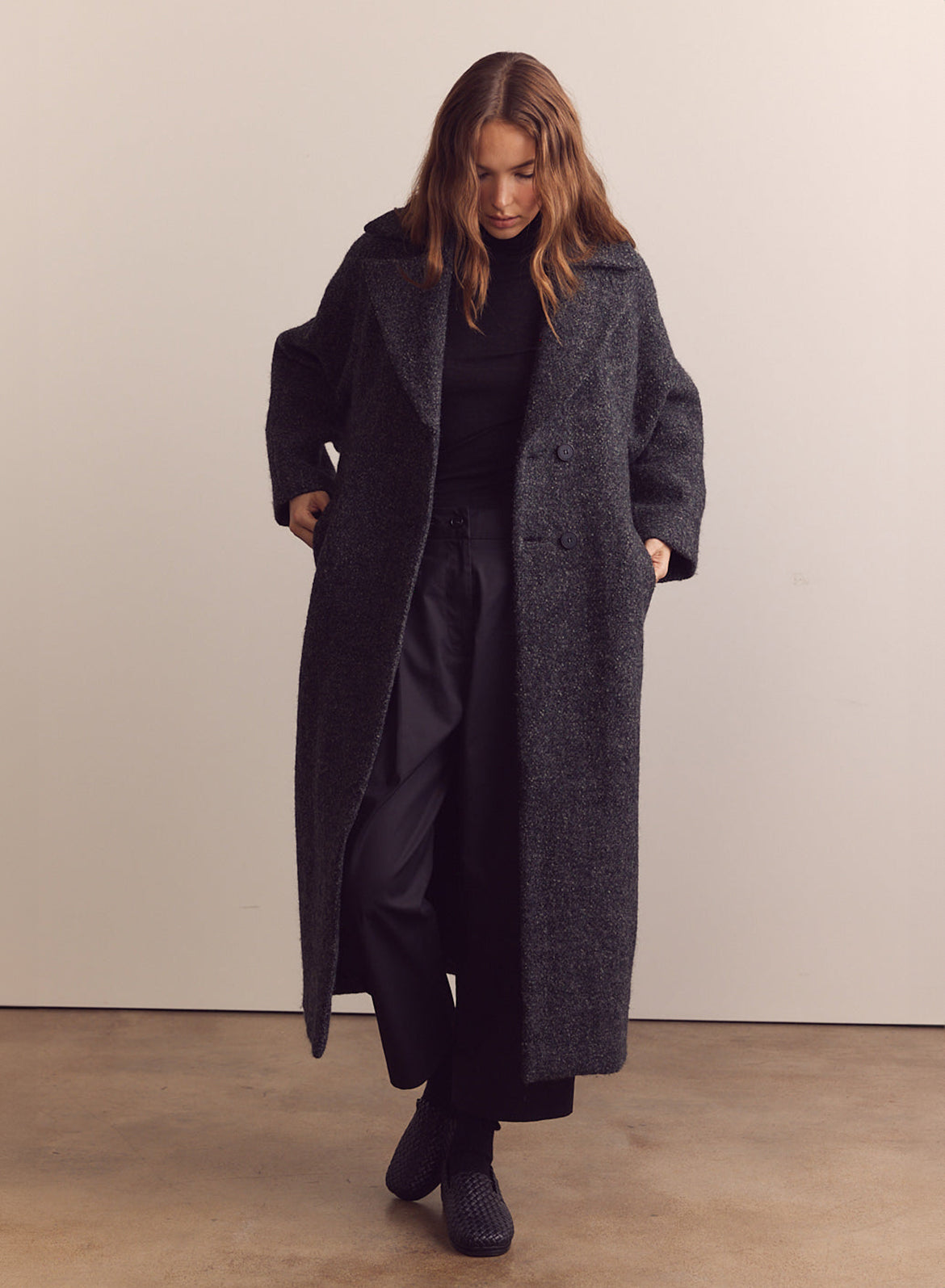 A woman wearing a long wool coat in dark grey speckled wool.