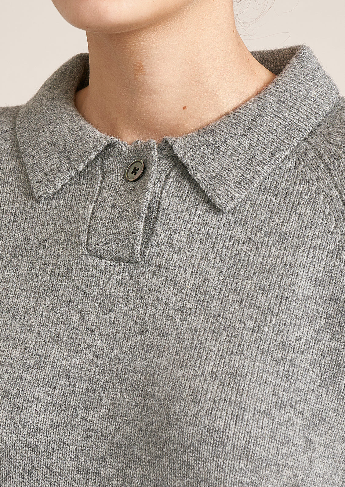 A woman wearing a heather grey long sleeve sweater with polo collar and button detail.