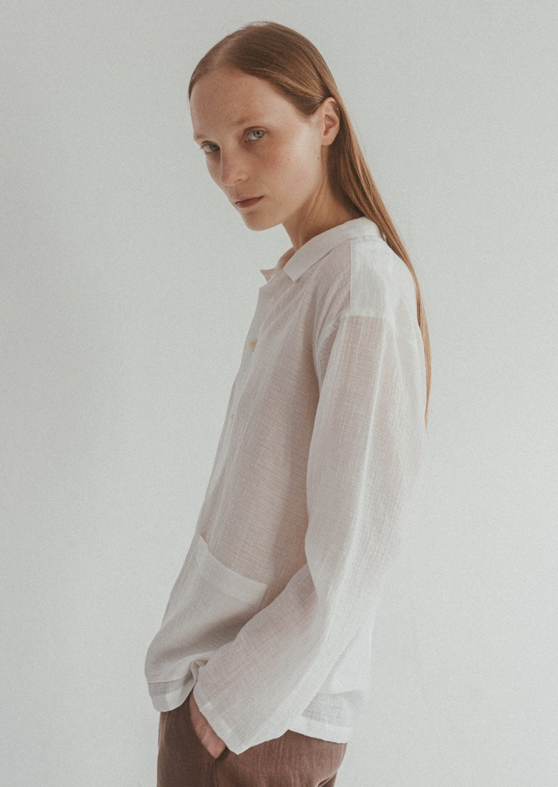 A woman wearing a semi-sheer, gauze-textured white button front shirt.