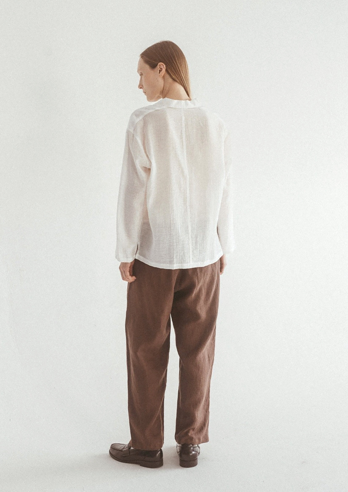A woman wearing a semi-sheer, gauze-textured white button front shirt.