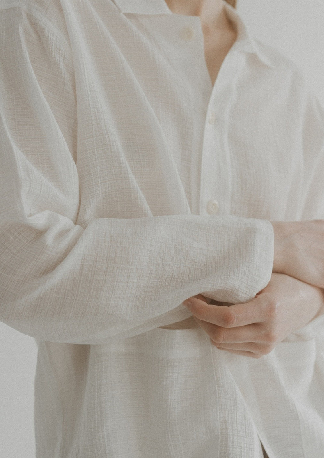 A woman wearing a semi-sheer, gauze-textured white button front shirt.