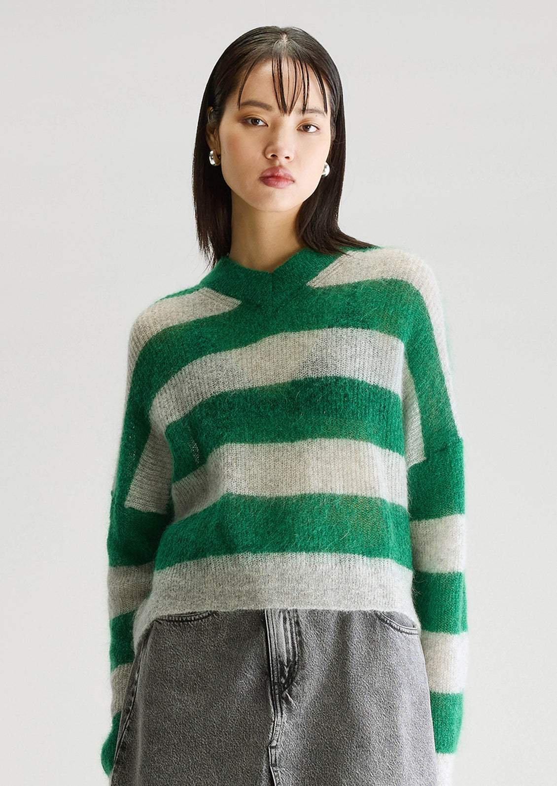 A woman wearing a mohair sweater in green and grey big stripes, with high v-neck.