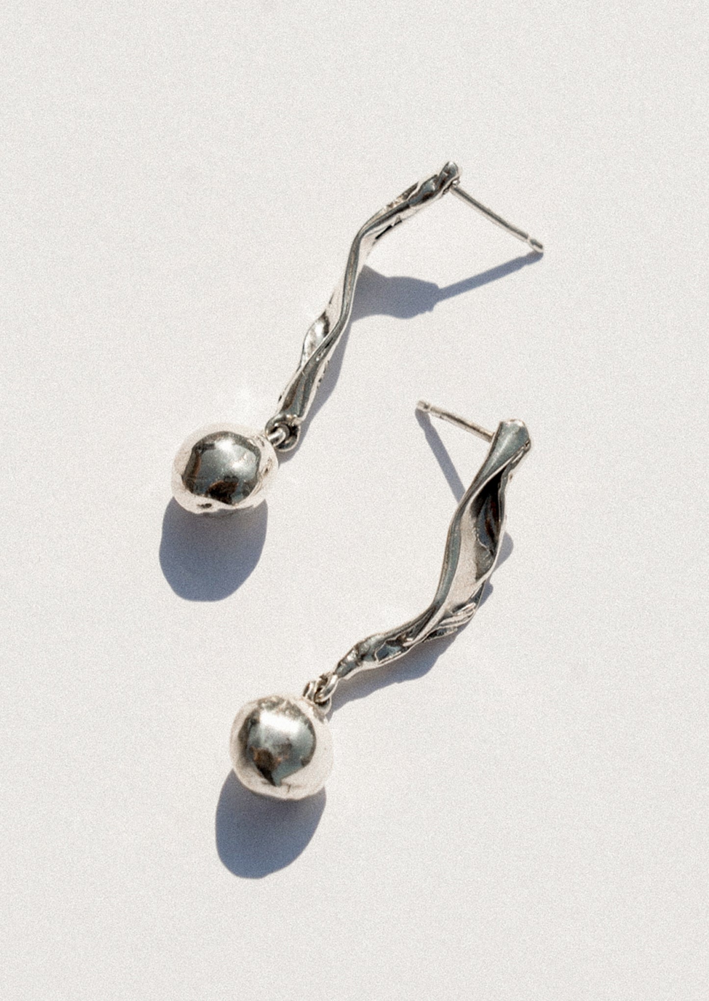 A pair of silver dangle earrings with twisted wire details and small polished spherical beads, photographed on a light gray background with sharp shadows.