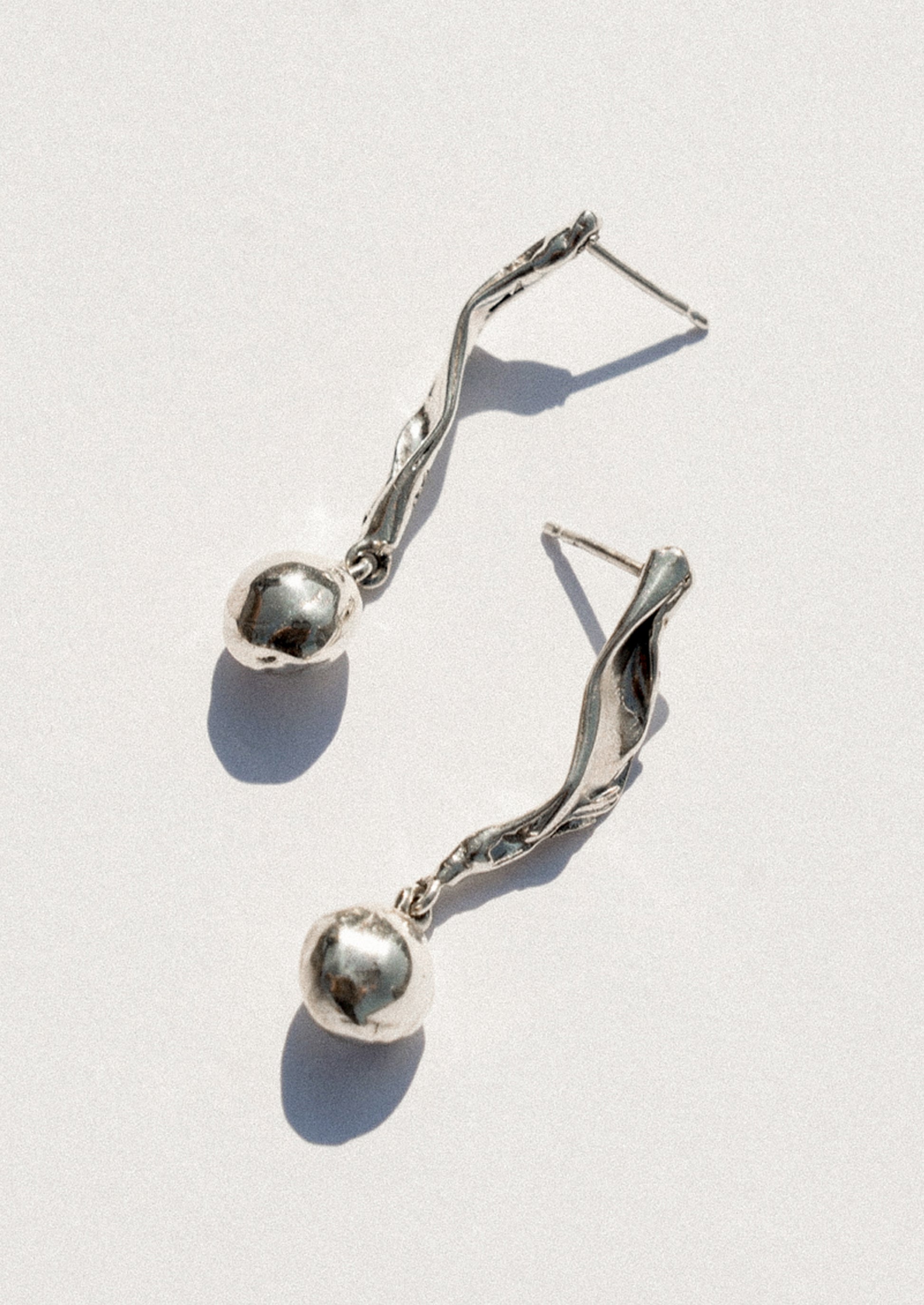 A pair of silver dangle earrings with twisted wire details and small polished spherical beads, photographed on a light gray background with sharp shadows.