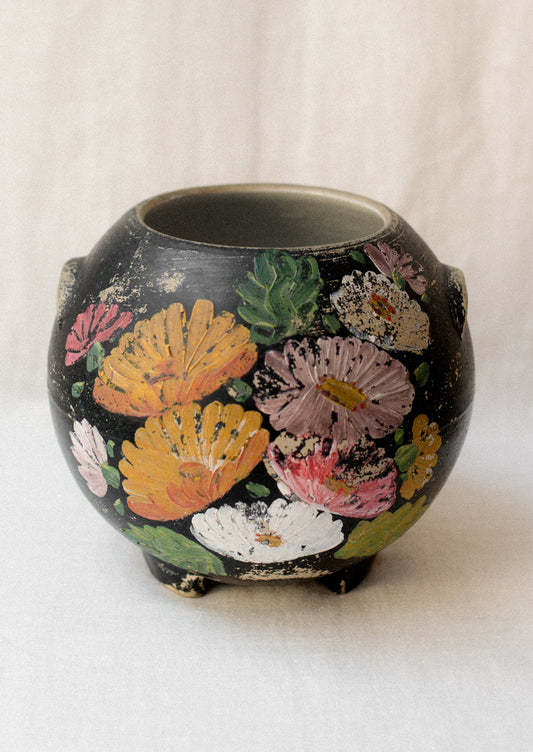 A black lidless round crock with multicolor aster flower pattern.