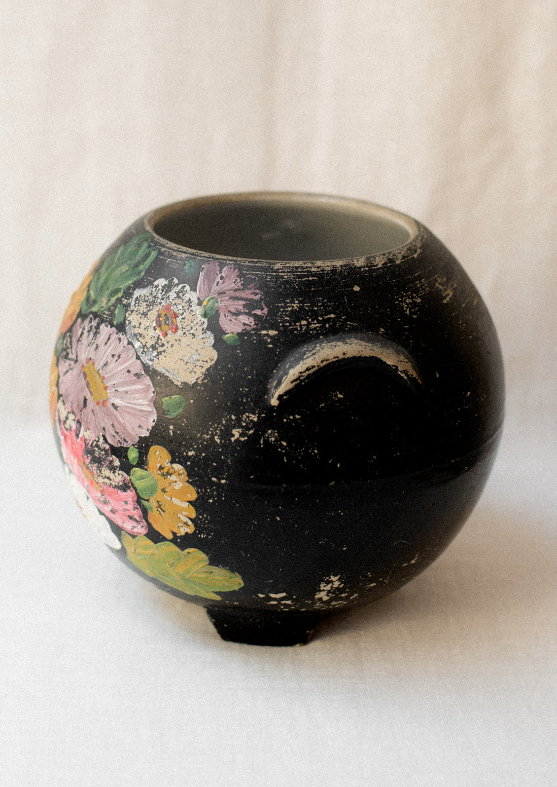 A black lidless round crock with multicolor aster flower pattern.