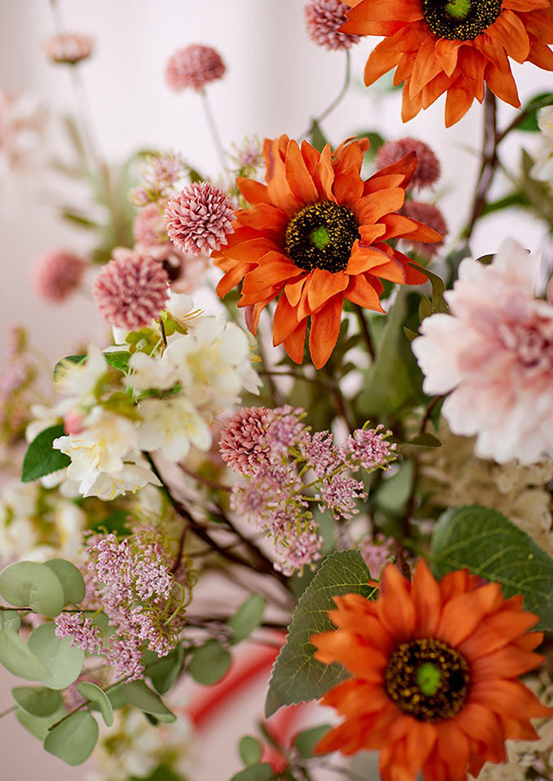 A faux flower arrangement with pink flowers and orange sunflowers.