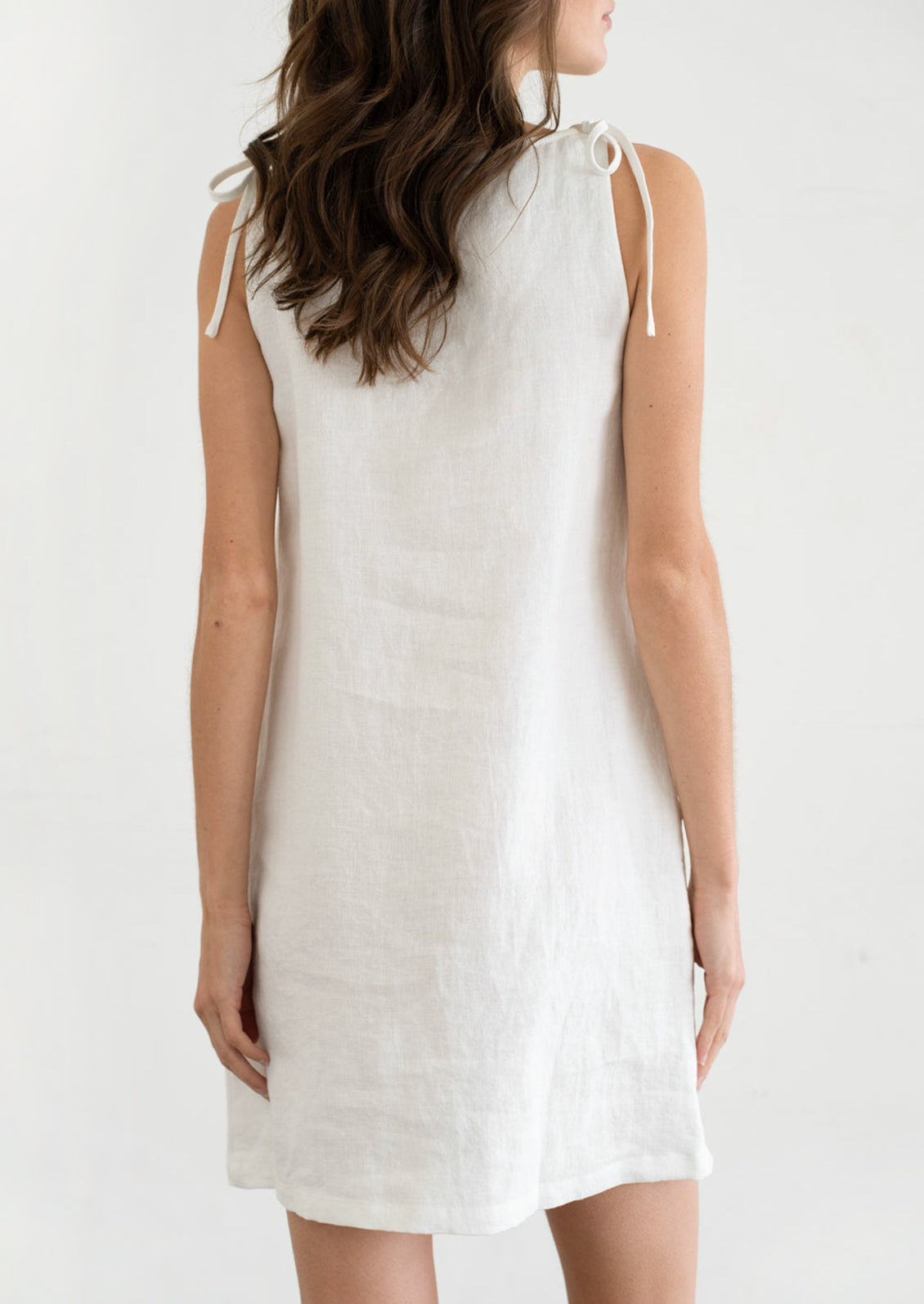 A person wearing an A-line mini dress in white with ties at shoulders.