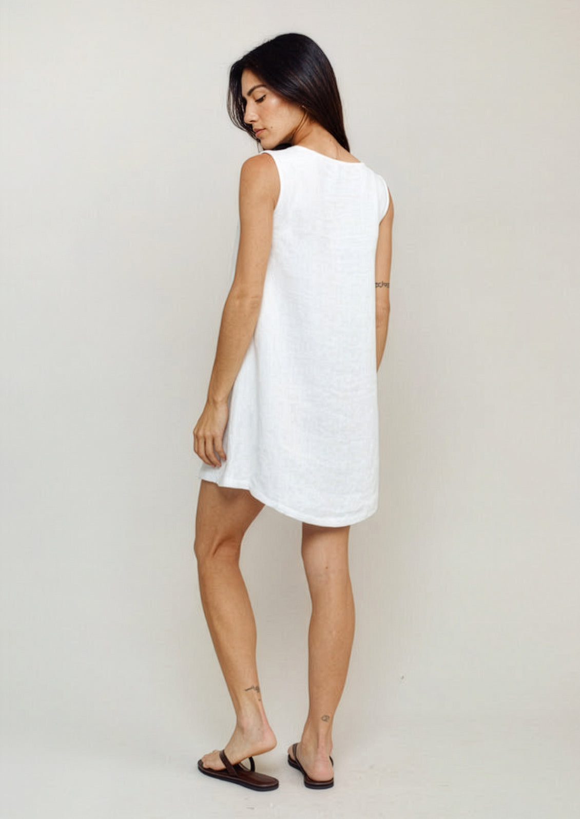 Woman wearing a white sleeveless dress against a plain background