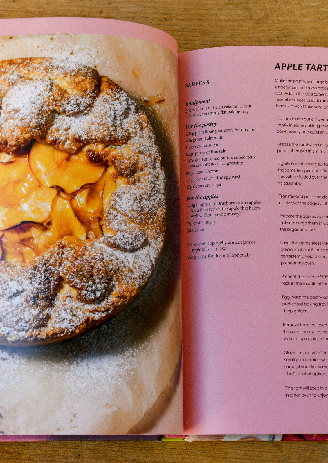 A cookbook open on a wooden table with a recipe for apple tart.