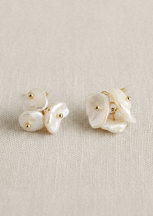 A pair of gold earrings with three freshwater pearls on each earring, set on a canvas fabric.