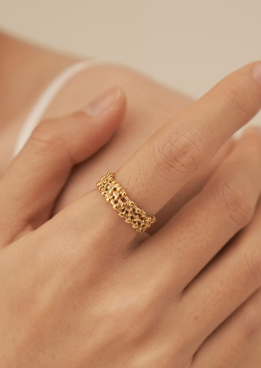 A person wearing a gold ring with thick woven textured band.