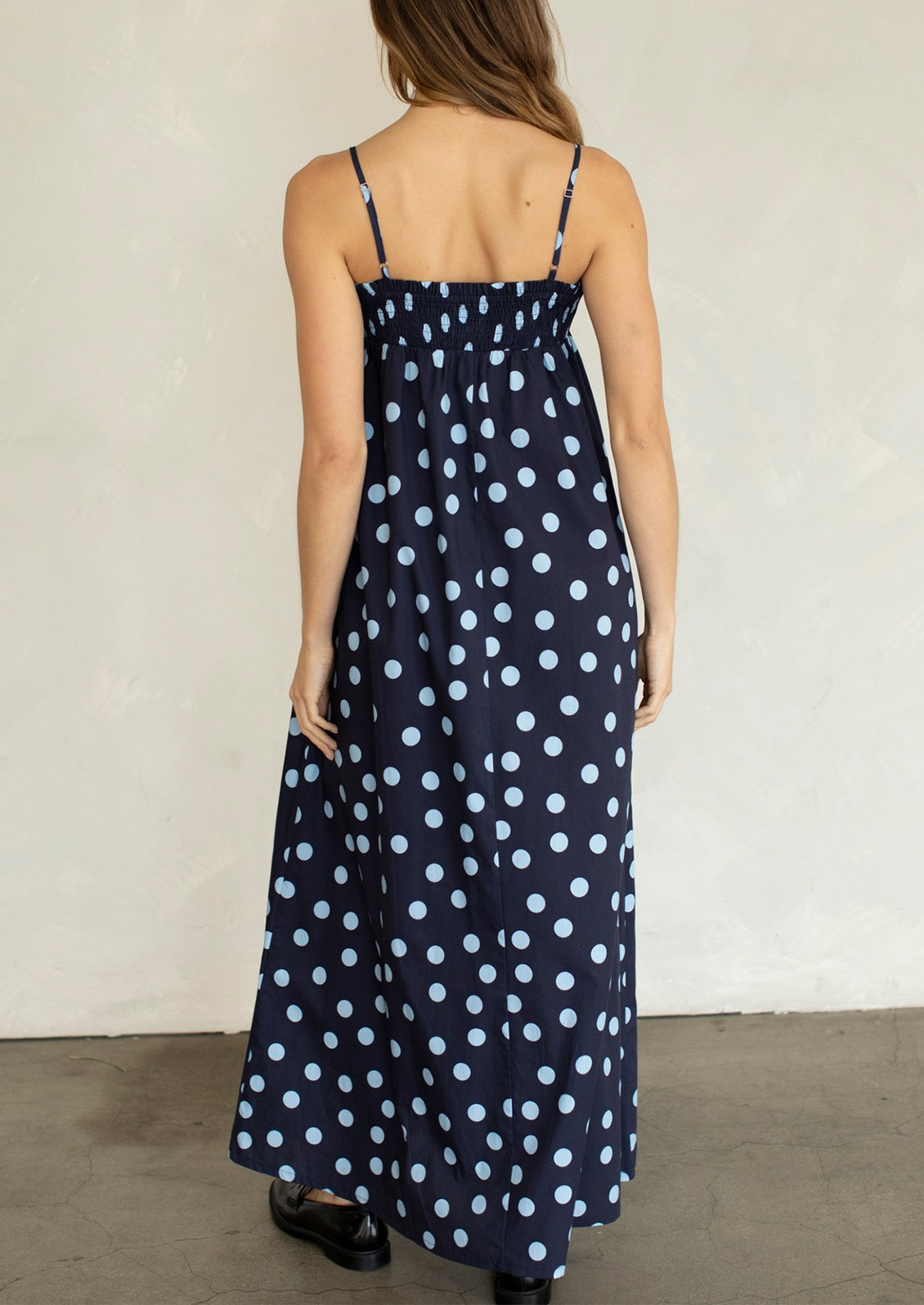 Woman wearing a navy blue dress with white polka dots against a plain background