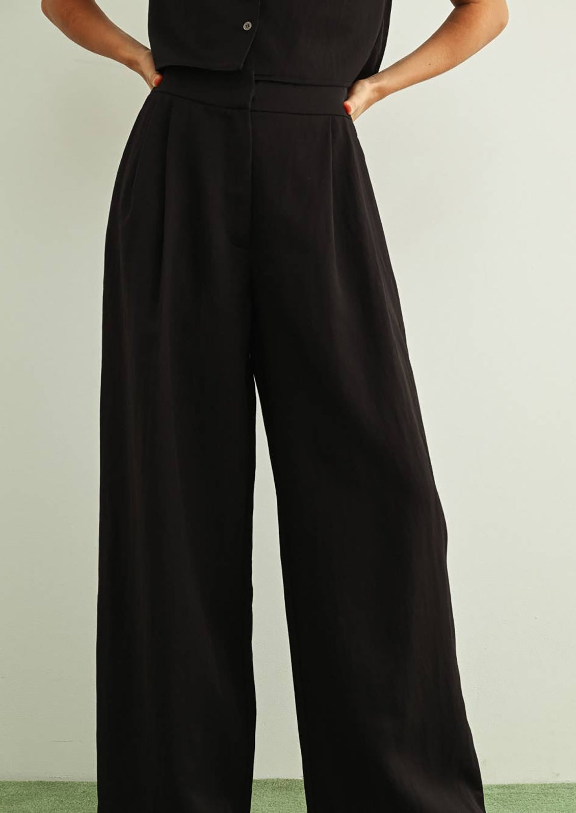 Person wearing a black jumpsuit with wide-leg pants on a light green background