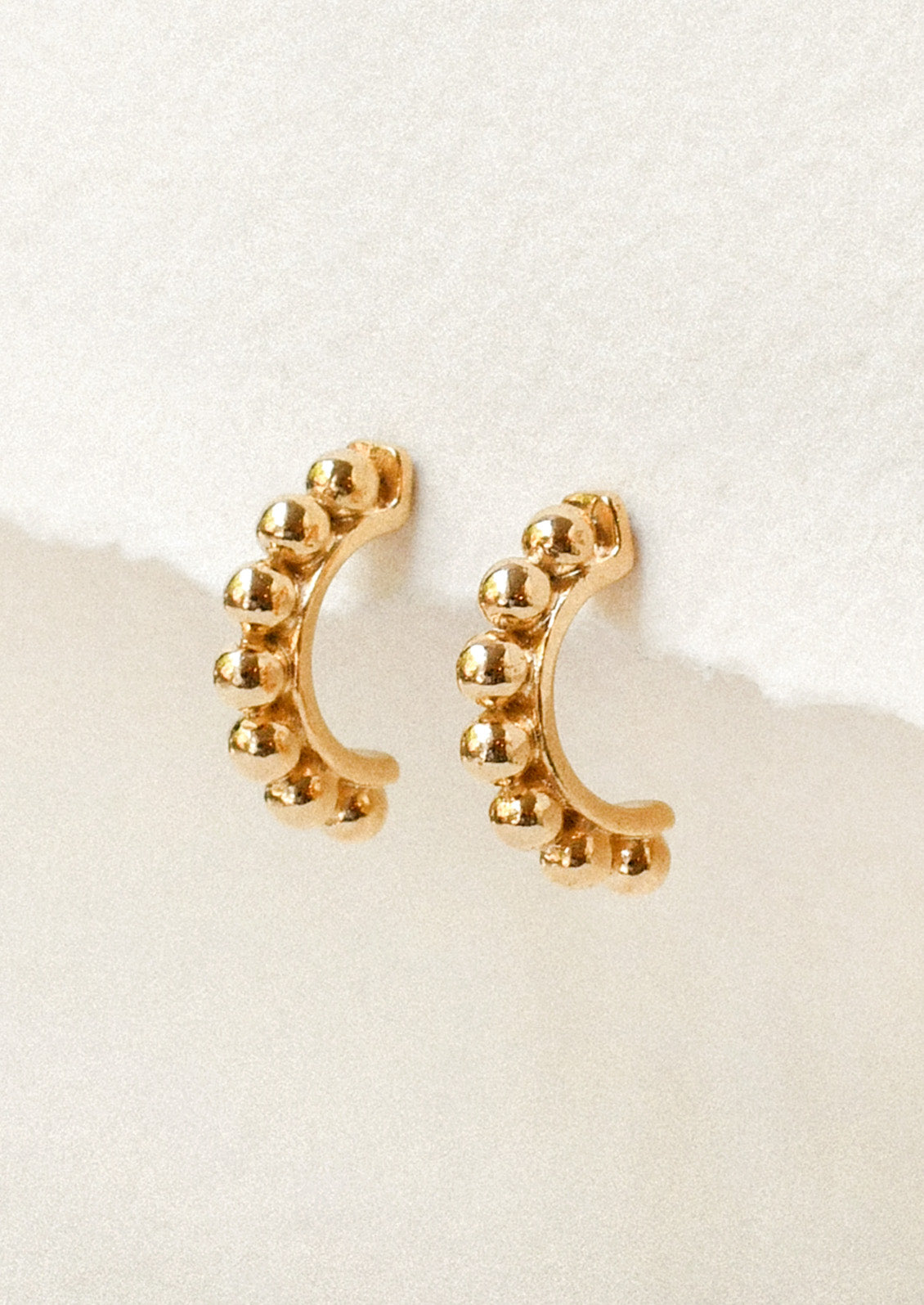 A pair of gold half hoop earrings with a beaded ball design along the tops.