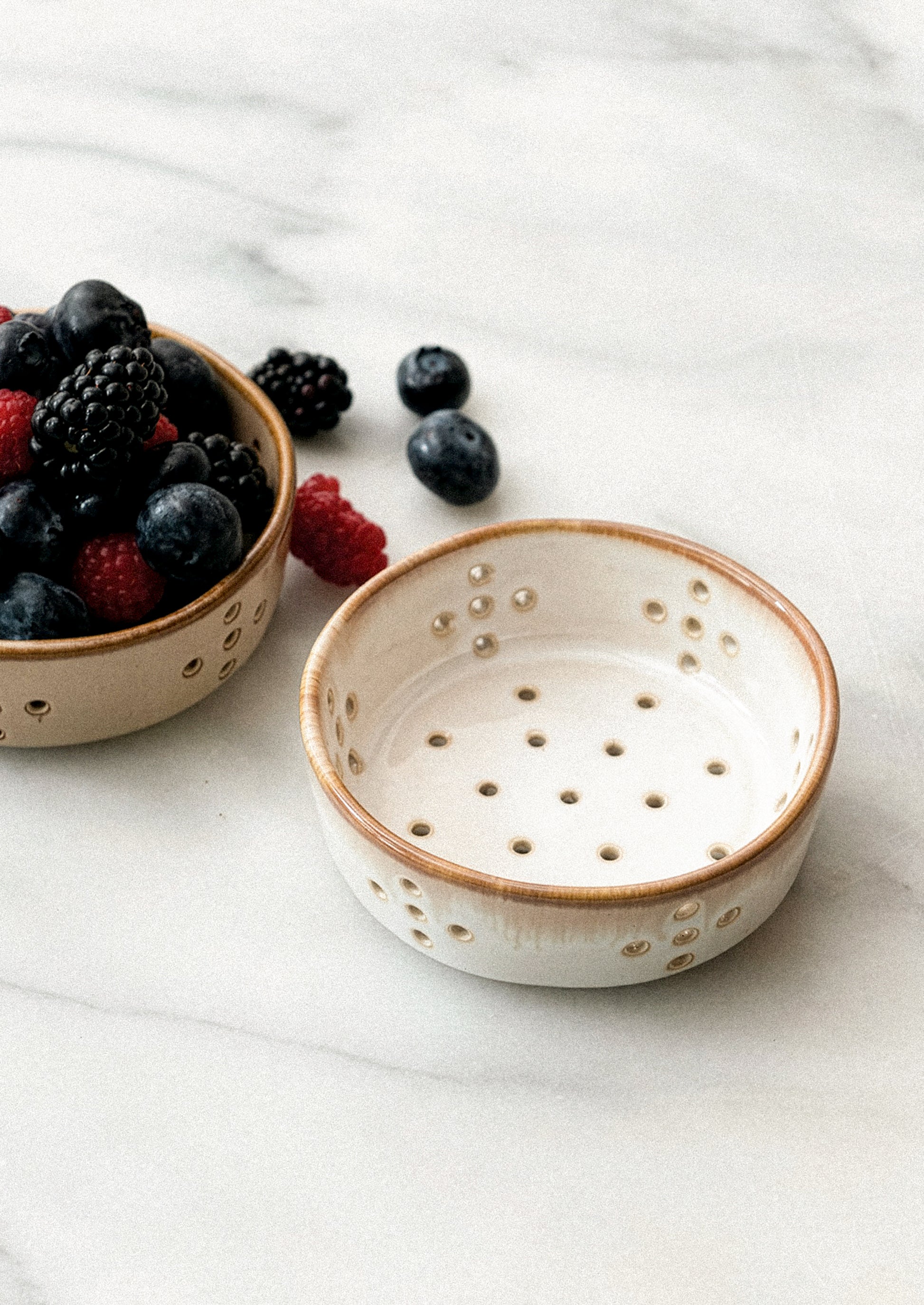 Small ceramic bowl with perforated design on a white surface with berries.