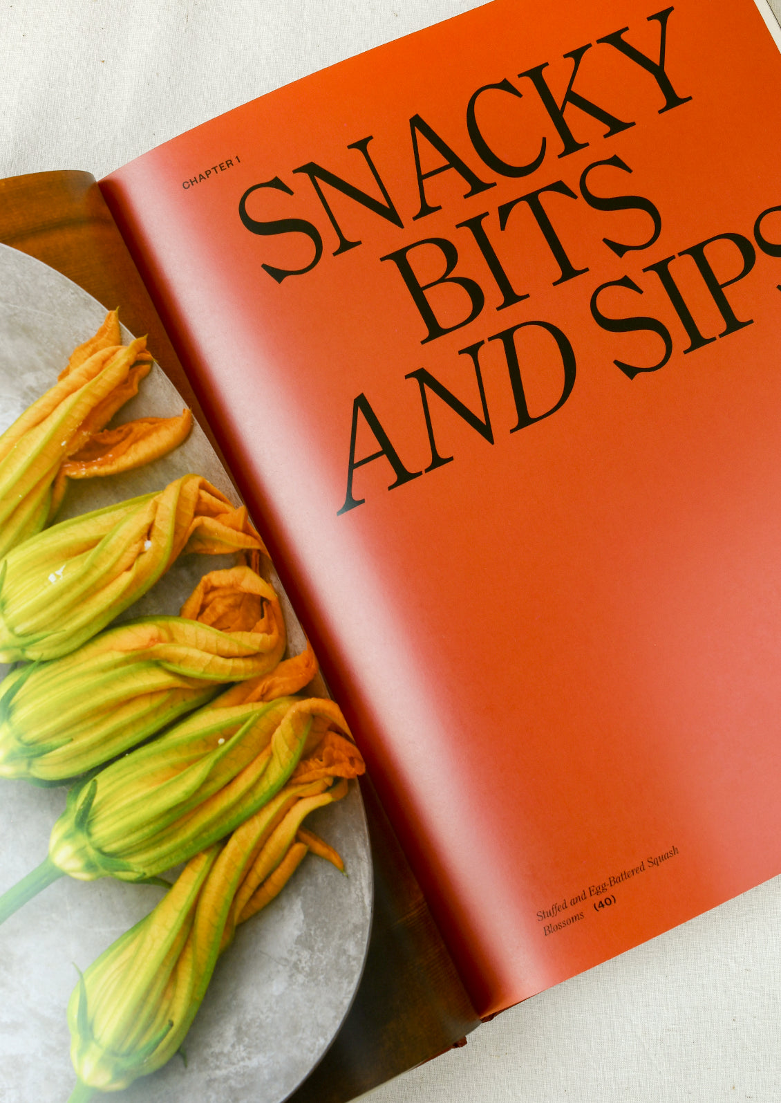 A cookbook open on a table with the headline "Snacky Bits and Sips"