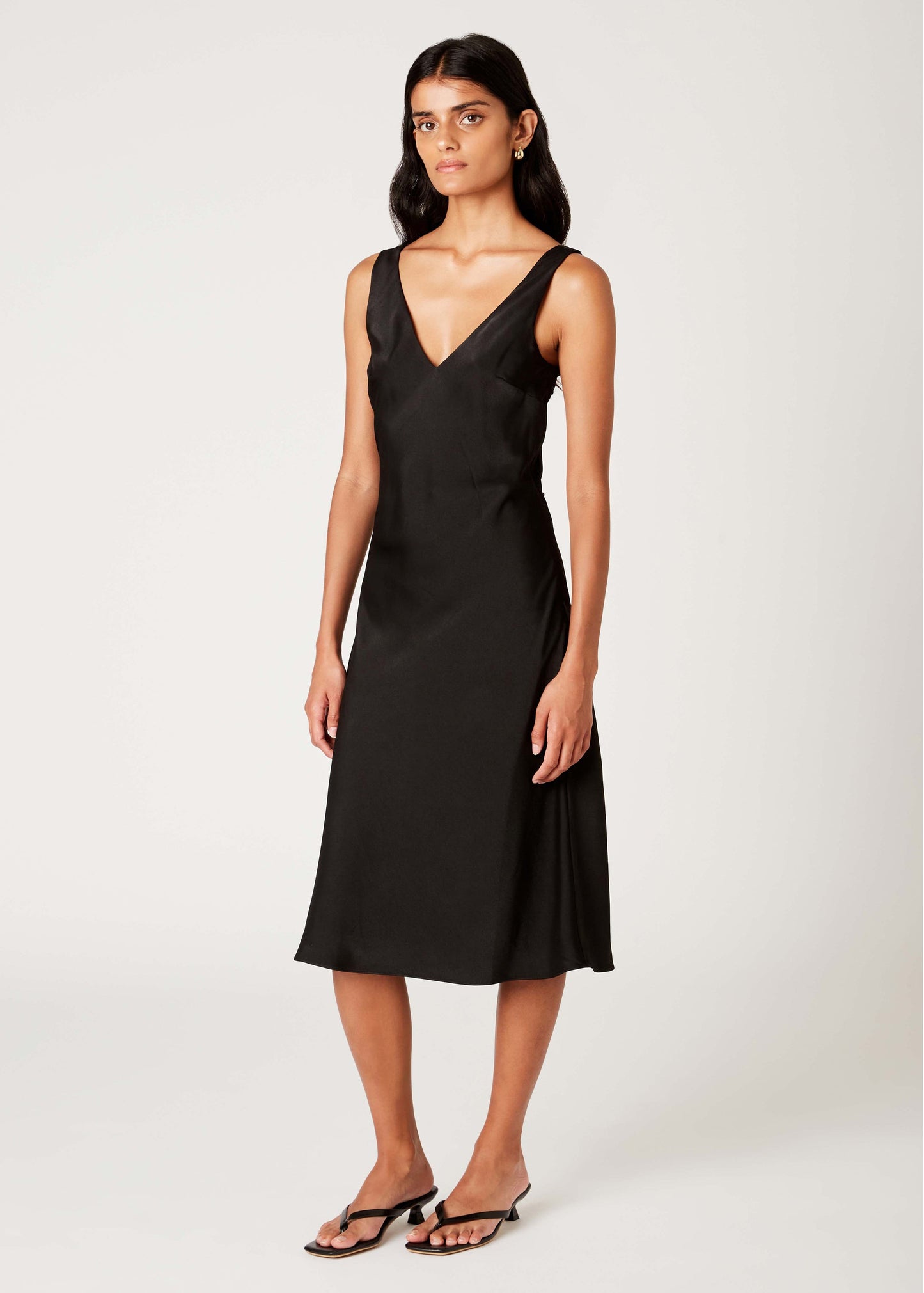 A woman wearing a satin v-neck sleeveless dress in black.