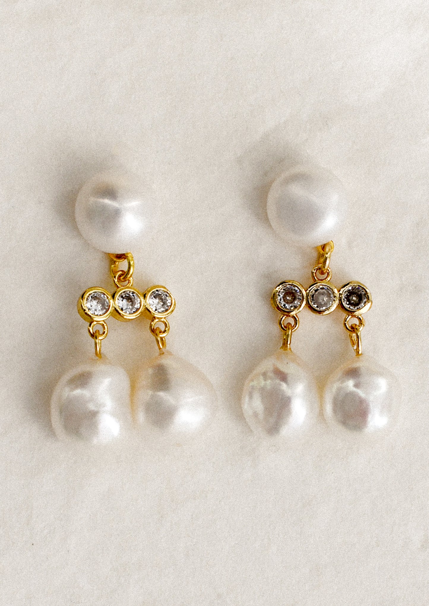A pair of stacked pearl drop earrings with triple crystal bar at center, in gold.