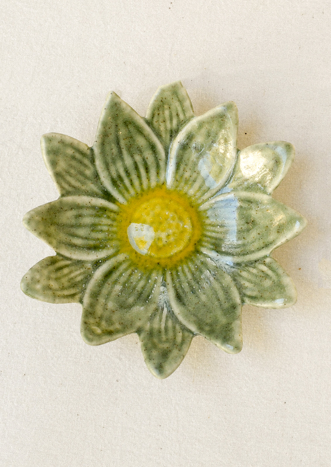 A small ceramic catchall dish in the shape of a flower in green with a yellow center.
