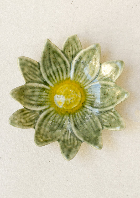 A small ceramic catchall dish in the shape of a flower in green with a yellow center.