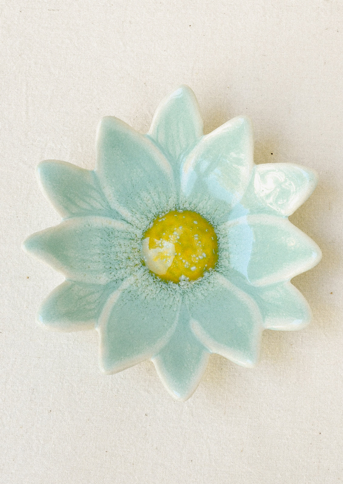A small ceramic catchall dish in the shape of a flower in sky blue with a yellow center.