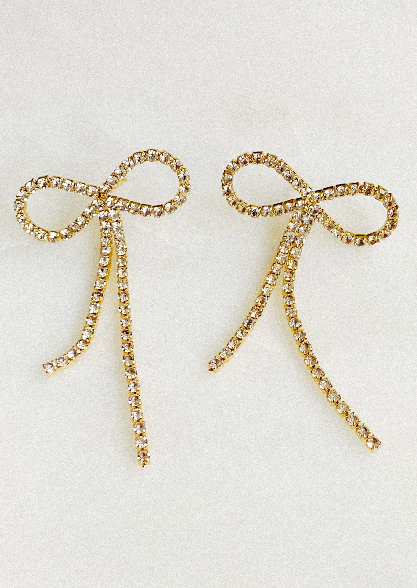 Gold bow-shaped earrings with rhinestones on a light gray background