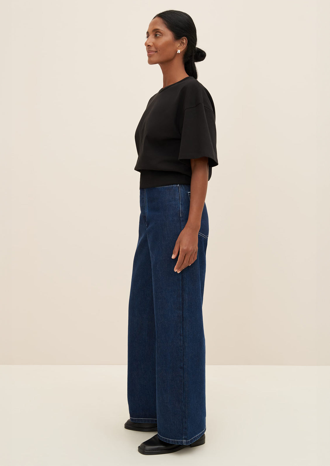 A woman wearing a boxy tee with short sleeves and fitted ribbed waistband, in black.