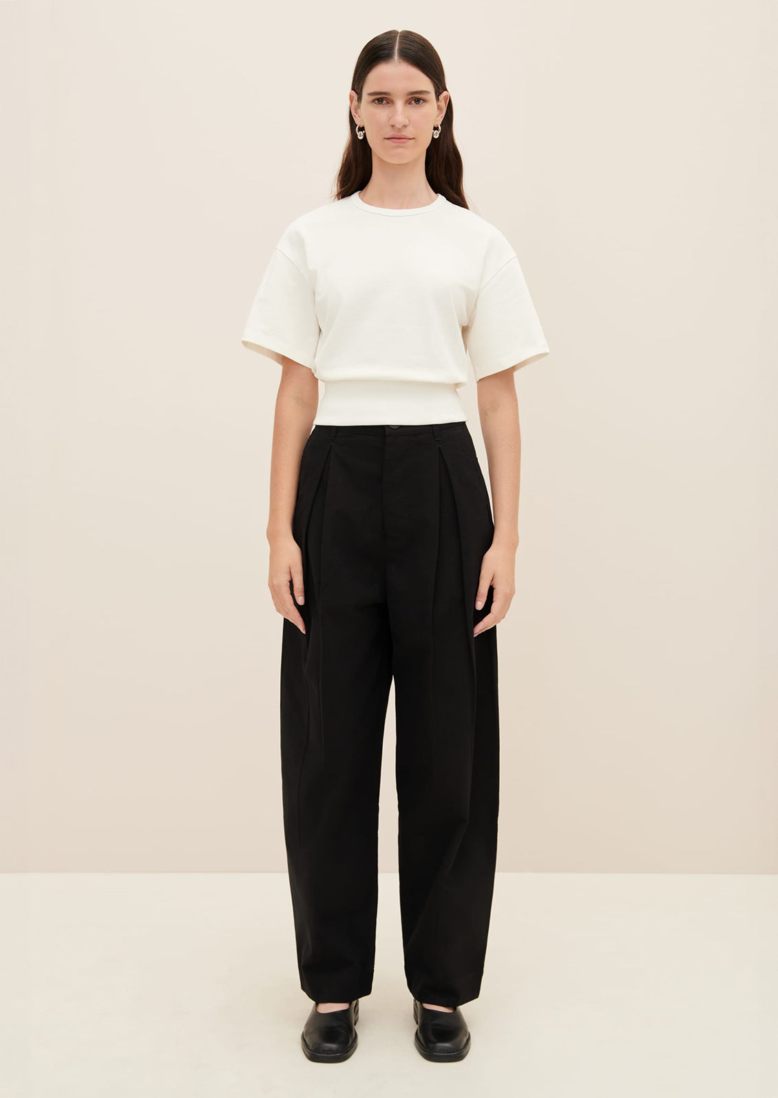 A woman wearing a boxy tee with short sleeves and fitted ribbed waistband, in white.