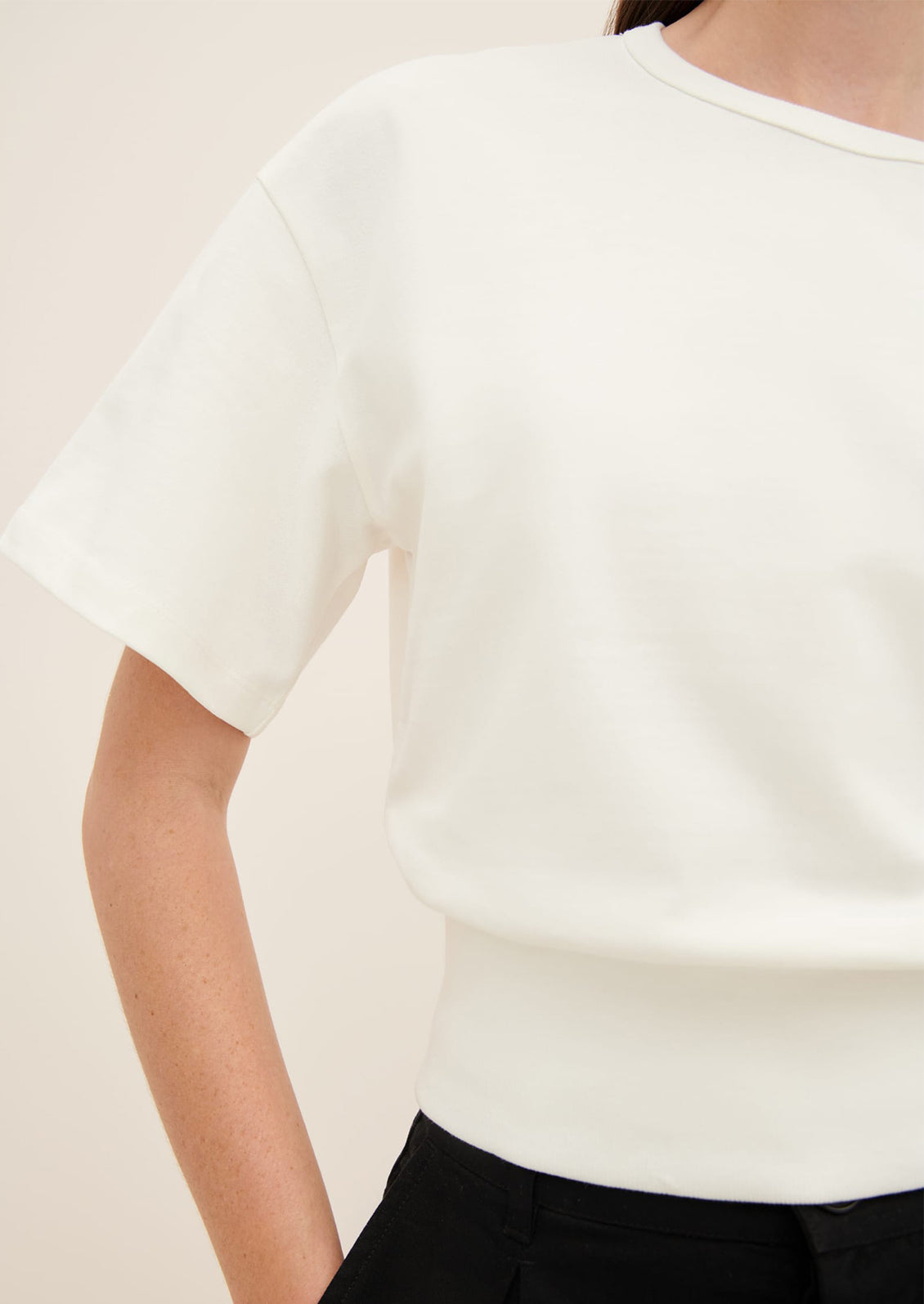 A woman wearing a boxy tee with short sleeves and fitted ribbed waistband, in white.