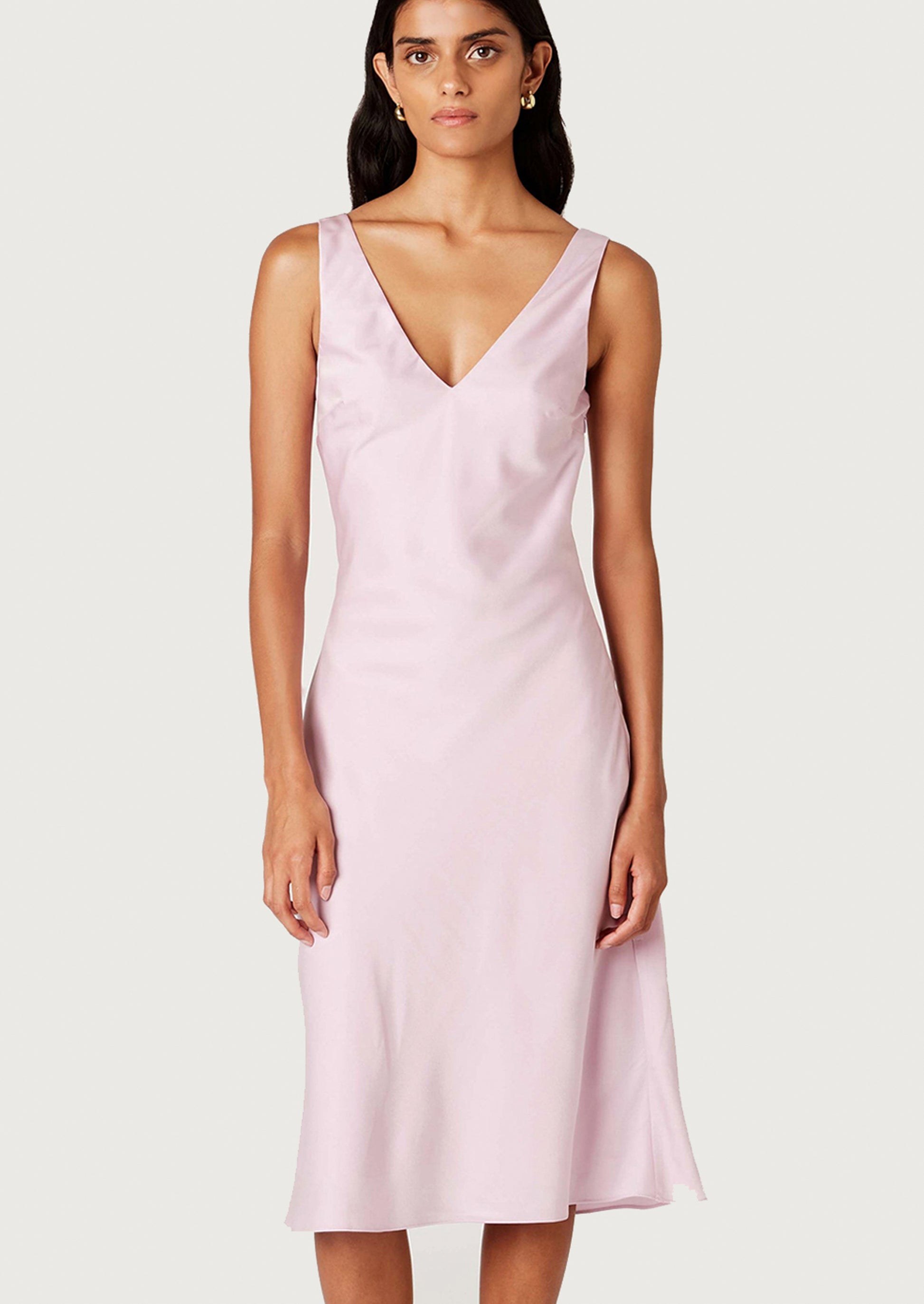 A woman wearing a satin v-neck sleeveless dress in ice pink.