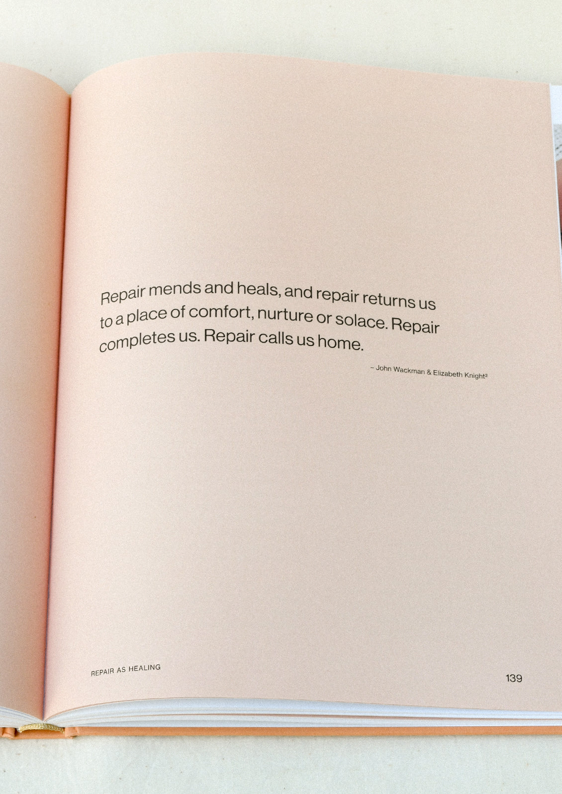 A book open on a table showing a page with a salmon colored background and a quote in black text.
