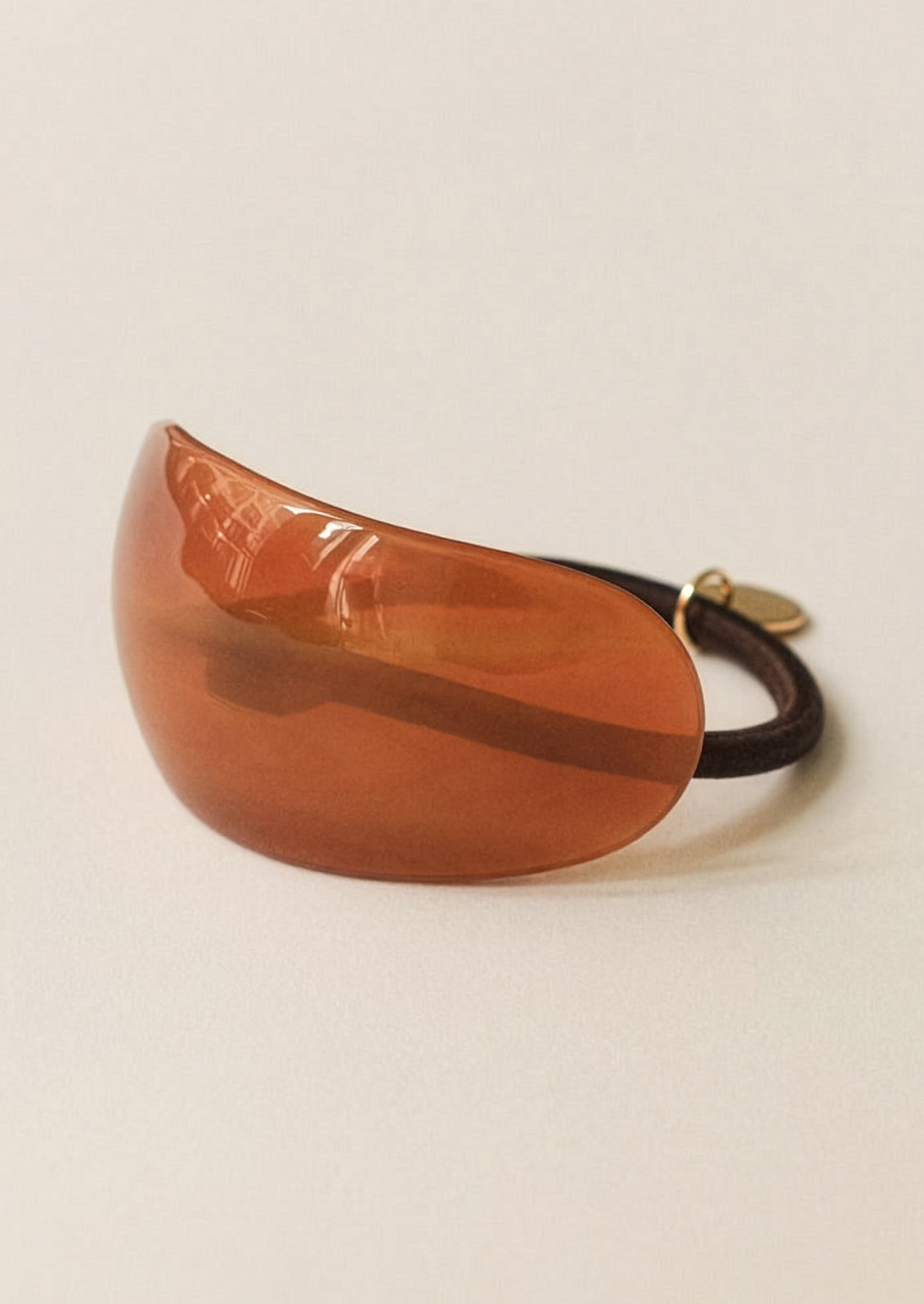 Brown hair tie with a gold clasp on a beige background