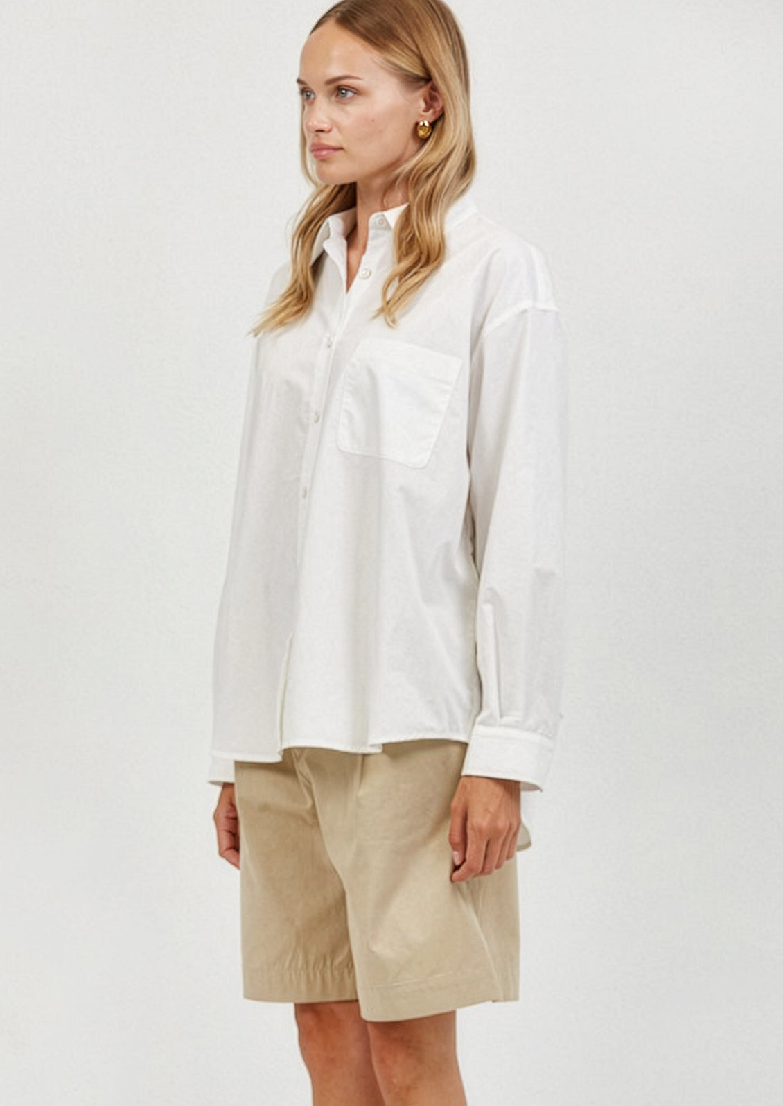 Woman wearing a white shirt and beige shorts on a plain background