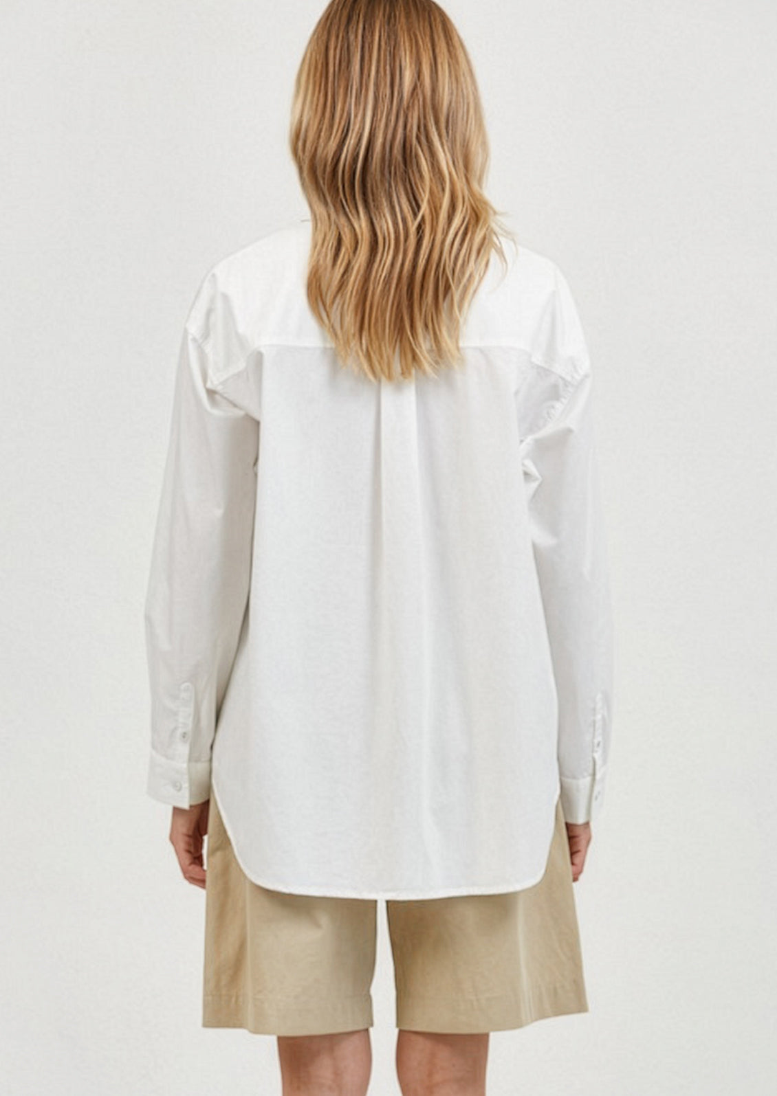 Person wearing a white shirt and beige shorts on a plain background