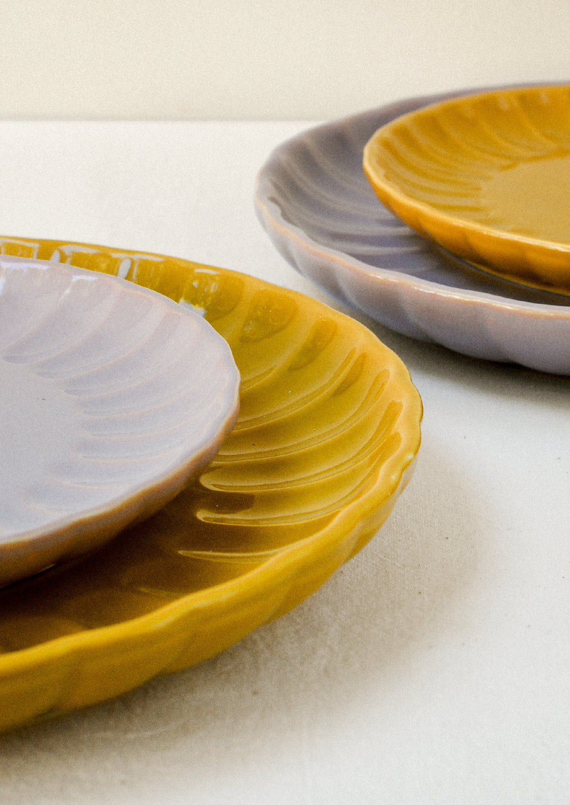 Mustard yellow and lavender ceramic plates stacked together, both with scalloped edges and glossy finishes.