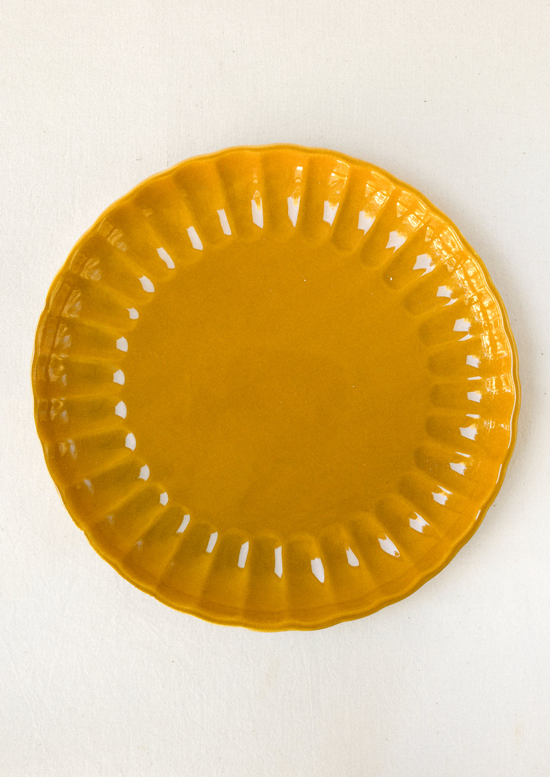 Mustard ceramic dinner plate with a scalloped edge and glossy finish, featuring a subtle ribbed pattern around the rim.