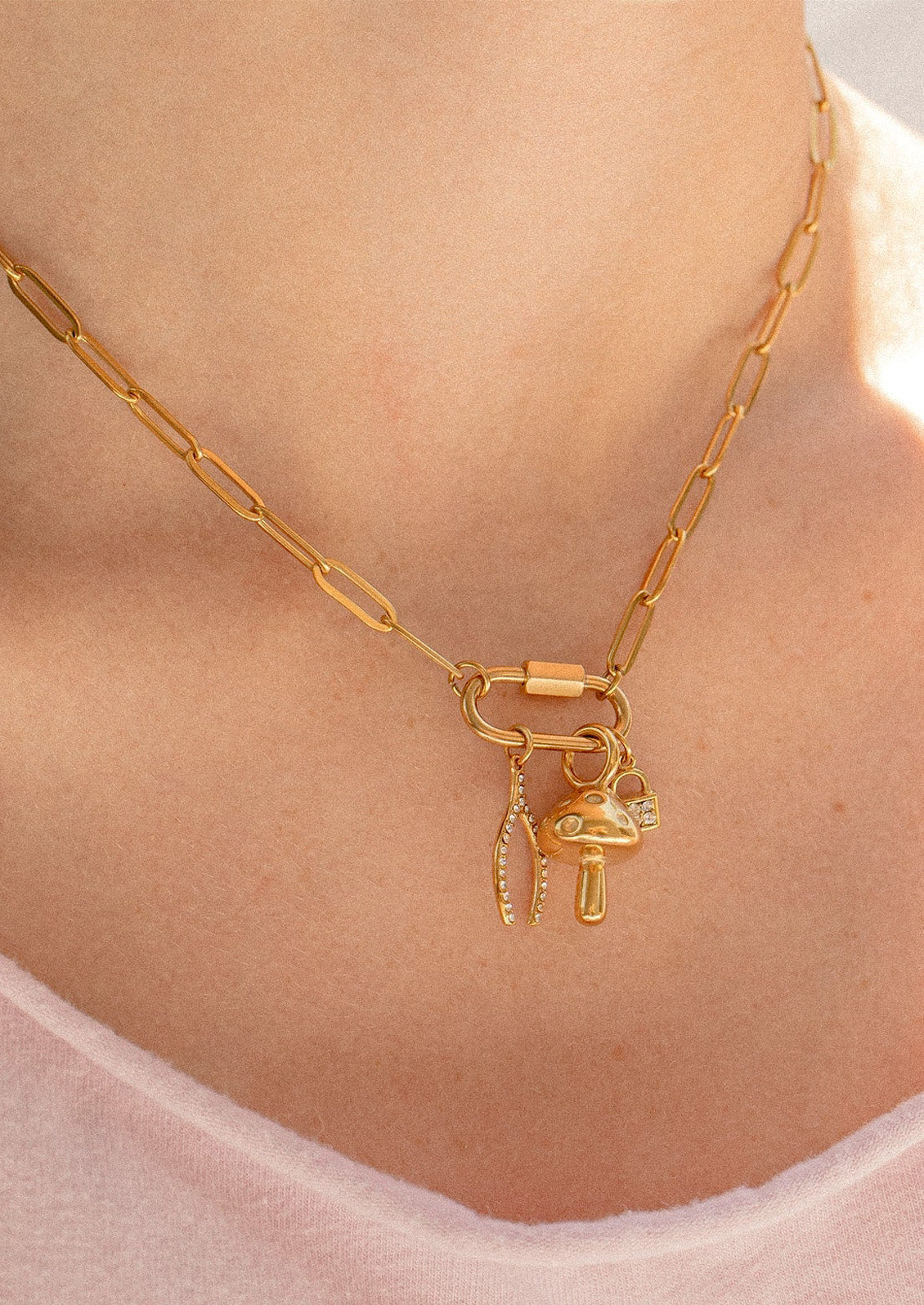 A woman wearing a gold chain necklace with a small carabiner and 3 small charms.