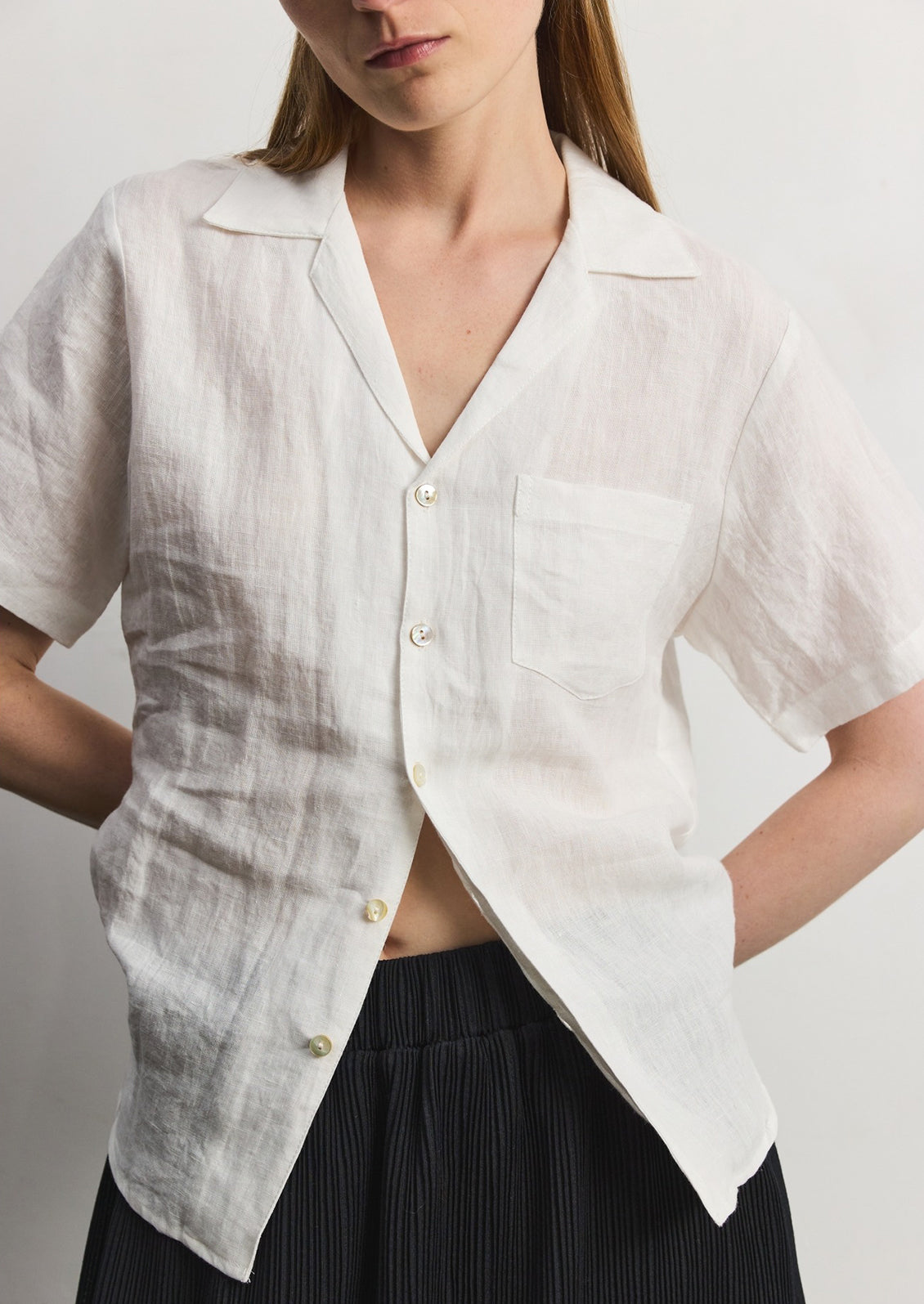 A woman wearing a white linen shortsleeved button-up. 