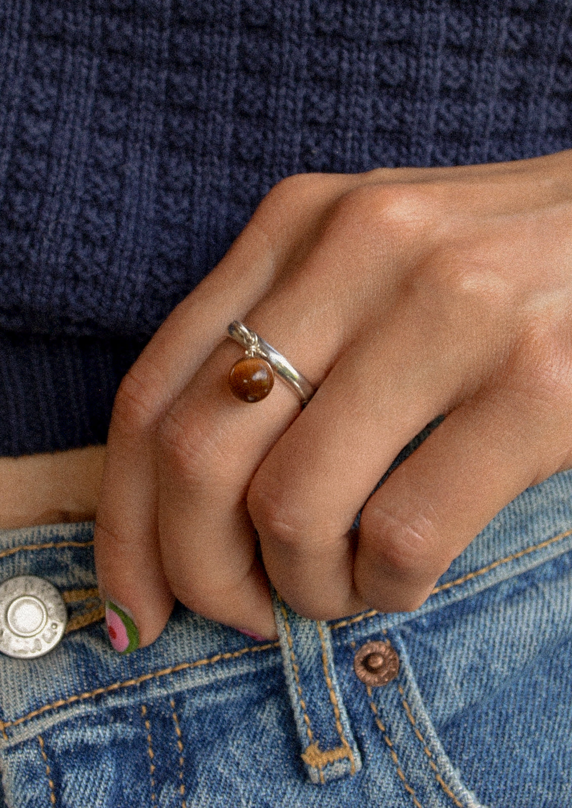 A woman wearing a sterling silver ring with a dangling coffee colored round charm.