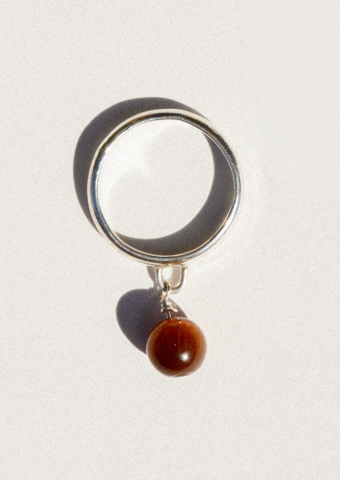 A sterling silver ring with a dangling coffee colored round charm.