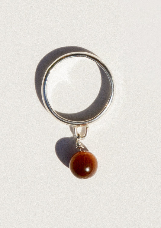 A sterling silver ring with a dangling coffee colored round charm.