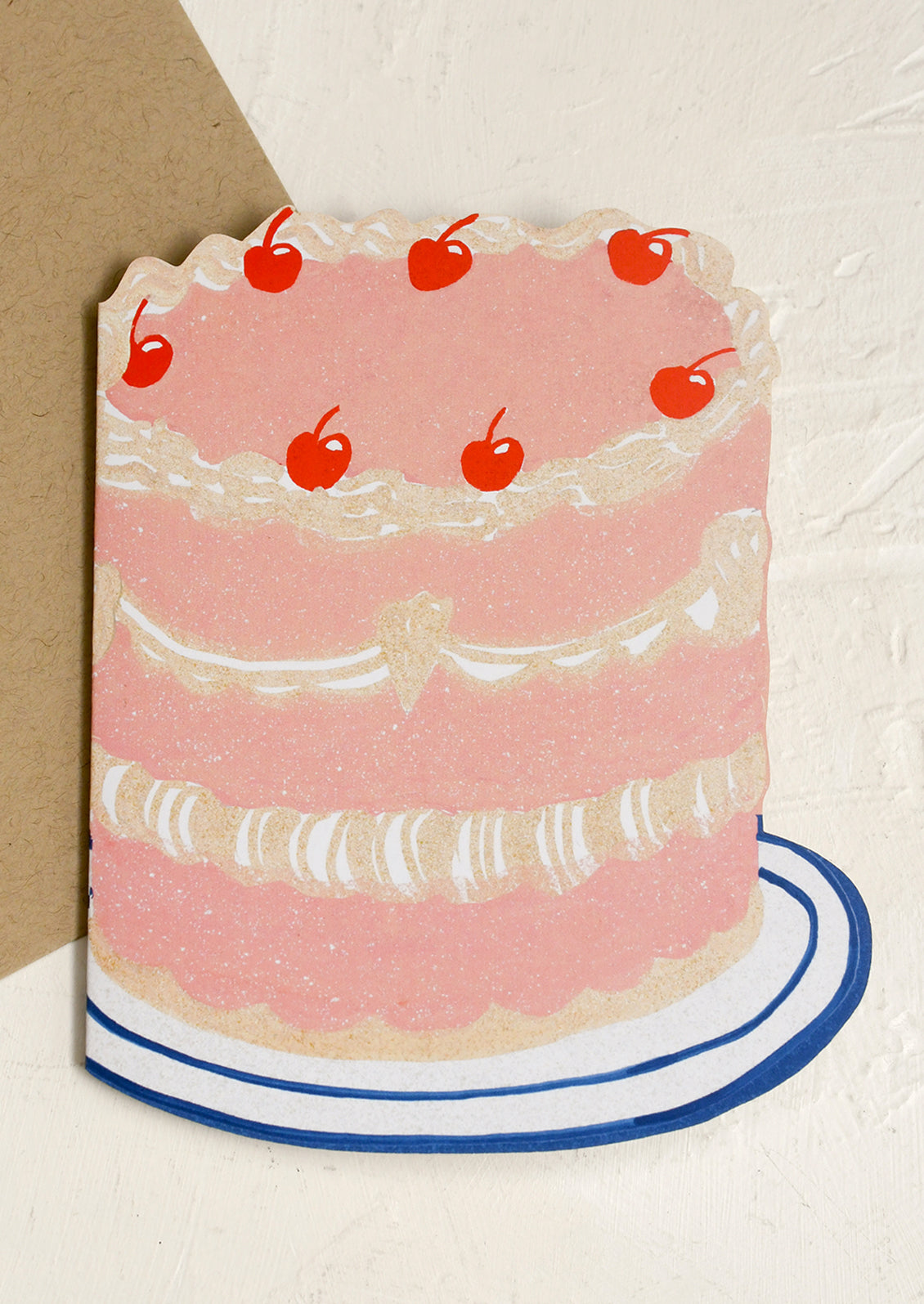 A diecut greeting card in the shape of 3 tier cake with cherries on top.