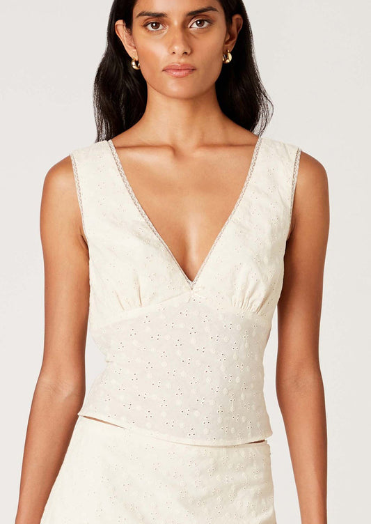 A woman wearing a sleeveless cotton eyelet lace top in cream, with deep v-neck.