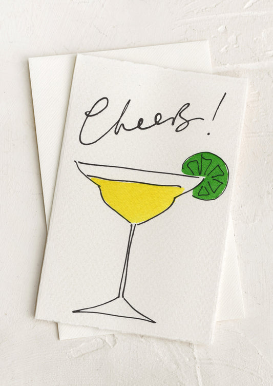A greeting card with hand painted illustration of a martini, text above reads "Cheers!".