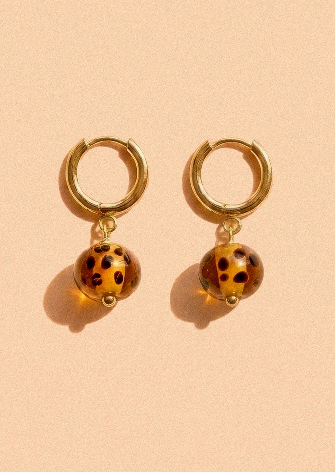 A pair of gold hoop earrings with cheetah print glass beads.