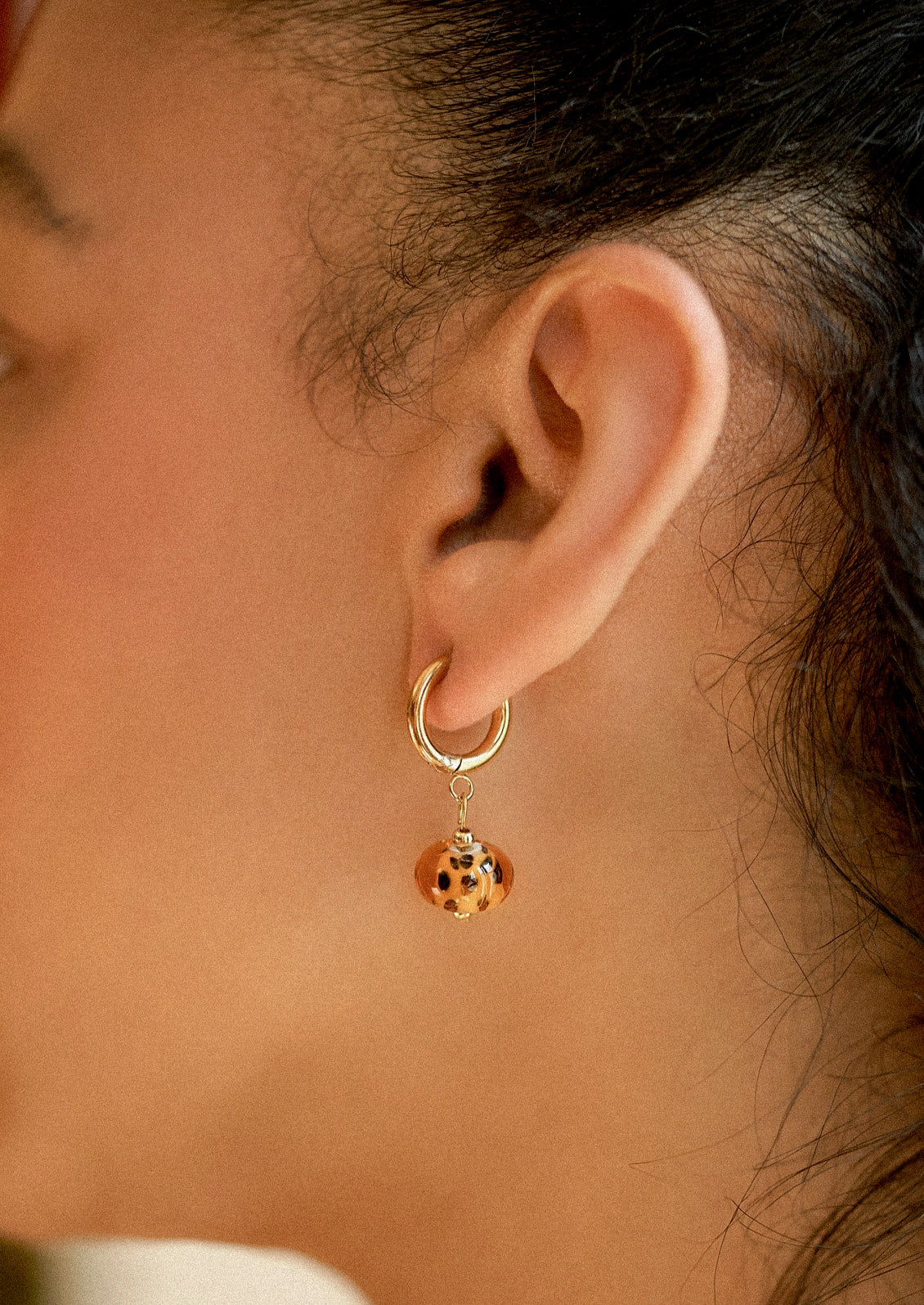 A woman wearing a gold hoop earring with cheetah print glass bead.