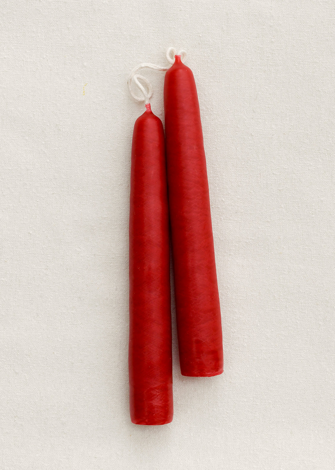 A pair of short red taper candles on a brown background.